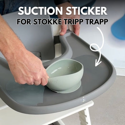 A man outdoors, lifting a wooden Stokke Tripp Trapp high chair using a strong suction bowl attached to it.
