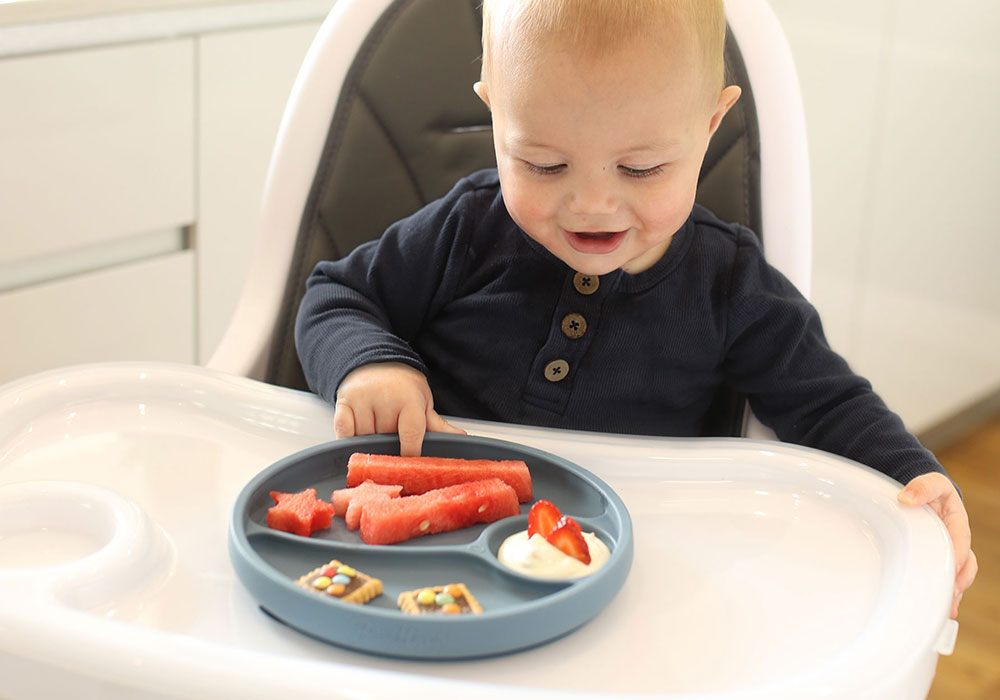 baby boy sitting in a high chair eating fruit from a silicone suction plate with dividers