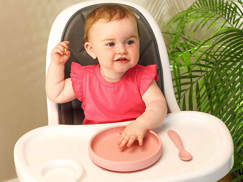 baby girl waiting for food ready in a high chair with pink suction plate and silicone spoon